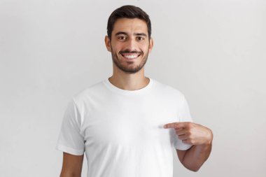 İşaret parmağı, kopya alanı için reklam, onun boş beyaz tişört gösteren gülümseyen güzel adam portresi yaz gri arka plan üzerinde izole
