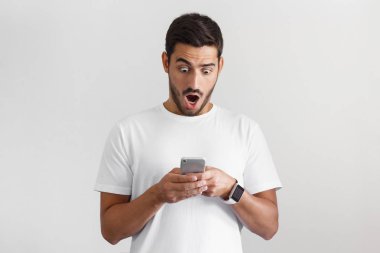 Genç adam, medya içeriği Web onun Smartphone ekranda tarafından etkilendim gri arka plan üzerinde izole portresi