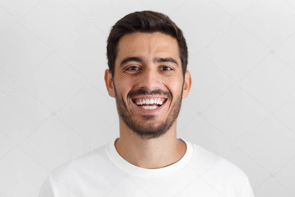 Close up shot of handsome smiling unshaven young man in white t-shirt laughing out loud