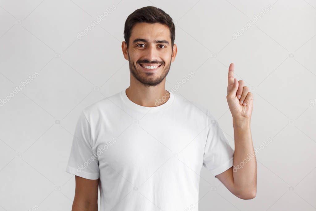 Handsome young man in white t-shirt pointing up with his finger isolated on gray background
