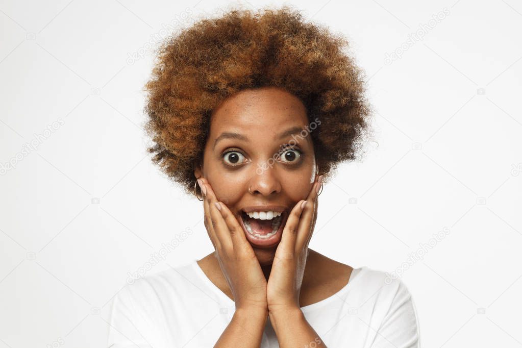 Young beautiful african american woman isolated on gray background, screaming happily in great astonishment with eyes and mouth open, palms pressed to her cheeks