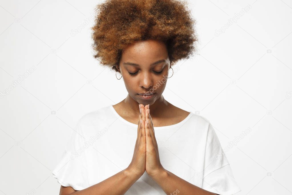 Closeup of young african american woman isolated on gray background putting hands together as if she is praying with closed eyes to overcome depression