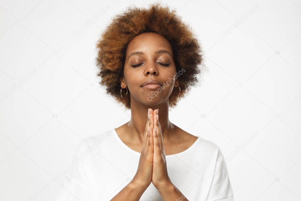 Beautiful young african american female isolated on gray background putting hands together as if she is praying with closed eyes 