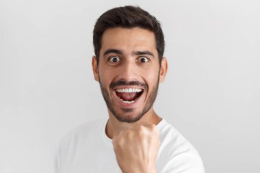 Onun takım kazanmak bağırarak genç çekici adam yumruk zafer jest, gri arka plan üzerinde izole olarak kaldırdı