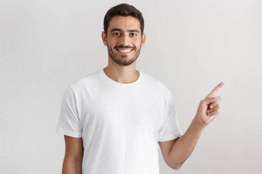 Beyaz t-shirt şu gri arka plan üzerinde izole parmağıyla işaret içinde genç adam