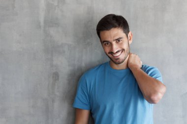 Güzellik atış genç gülümseyen adam rahat mavi t-shirt ayakta gri dokulu duvar karşı kapatın