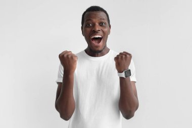 Zaferini kutluyor ve kazanan, mutluluk ve şans derin duygusal ifade Yumruklarını sıkma sanki hareket gri arka plan üzerinde izole bağırarak Afrikalı bir adam