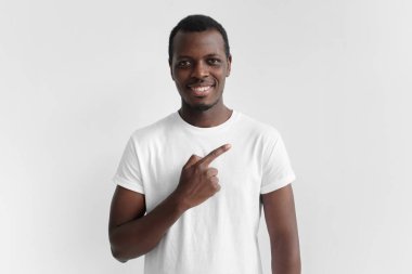 Yakışıklı genç Afro-Amerikan adam beyaz t-shirt şu gri arka plan üzerinde izole parmağıyla işaret