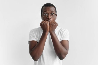 Portrait of scared young African American man keeping hands in fists, holding them in front of his face, looking at camera with shocked and frightened expression. Fear concept clipart