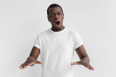 Beyaz t-shirt, gri arka plan üzerinde izole nedir genç Afro-Amerikan adam açık ağızlı dur hareketi her iki el ile gösterilen