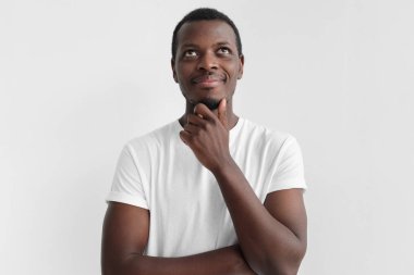 Düşünme, gri arka plan üzerinde izole genç Afro-Amerikan adamla rüya gibi neşeli ifade, gün ışığından yararlanma portresi