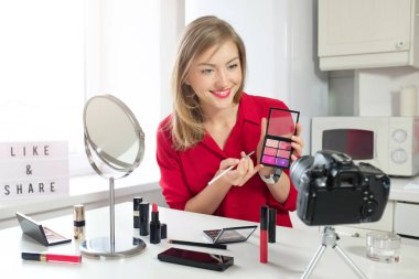 Renkli gösterilen kadın güzelliğinin vlogger makyaj paleti fırça ile video kamera için online, kapalı mutfak masada oturuyor. Canlı akışı. Hangi tarihlerde ve paylaşmak