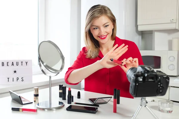 Beauty tips. Portrait of smiling young female blogger filming video for blog, sitting at kitchen table and showing cosmetics with beautiful smile. Best product concept