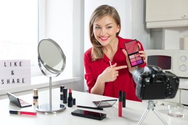 Yatay closeup onu güzellik blog abonelerine göstermek için en iyi renkleri gösteren kozmetik mutfak masası ve holding parlak dudak paleti, tak Avrupa Rus kadının genç gülümseyen