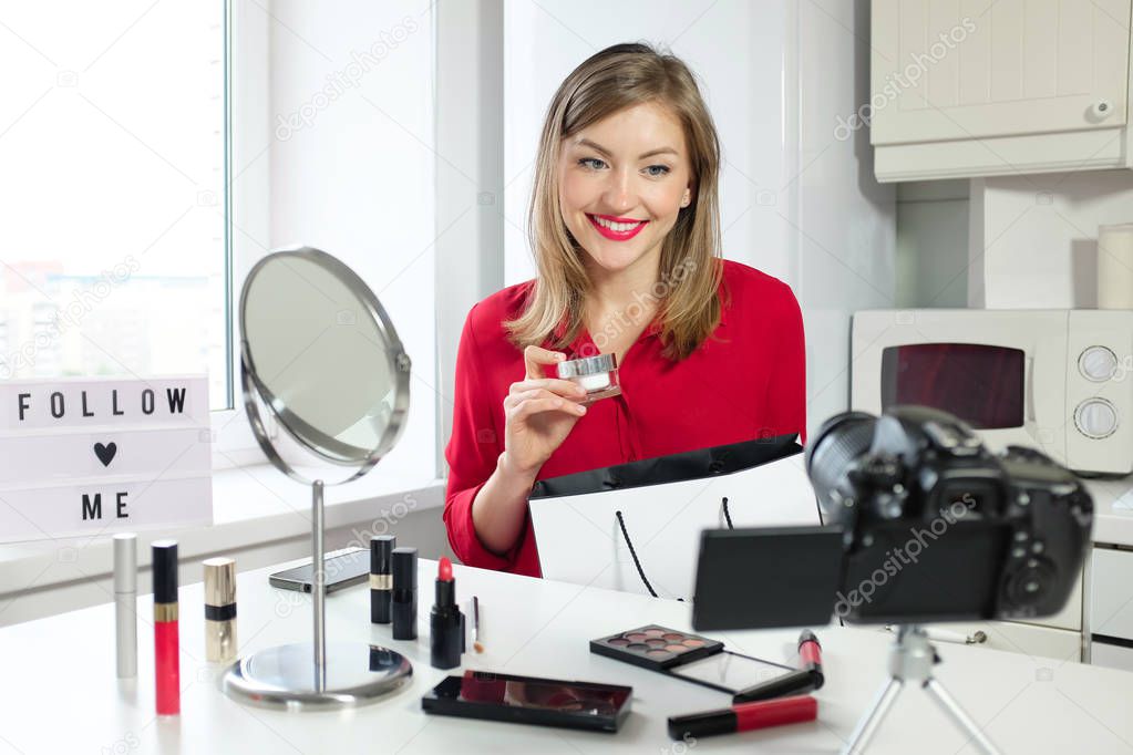 Horizontal closeup of young positive European Russian woman looking at camera standing on table, taking products out of paper bag, telling viewers of her beauty blog about things she has bought