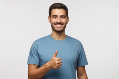 Genç başparmak olumlu duygular ve mutluluk ile gösterilmesini izole üzerinde gri arka plan adam. Memnuniyeti kalite ve tavsiye