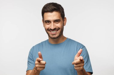 Genç adam gri arka plan açık ağız ile mutlu bir şekilde gülümseyerek ve kamera iki eliyle işaret eden mavi t-shirt giyen üzerinde izole 