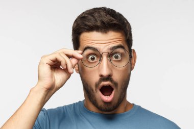 Young man in blue t-shirt shouting oh my god with open mouth, holding round glasses, surprised by low price and sales clipart