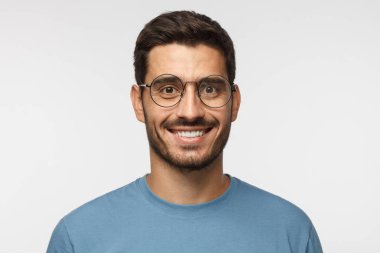 Çekici bir adam mavi t-shirt ve gri arka plan üzerinde izole trendy yuvarlak gözlük gülümseyen in atış kapatın