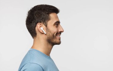 Genç adam müzik veya radyo, dinleme gülümseyen yana portresi mavi t-shirt giyen modern kablosuz kulaklık kullanır. Metin için yer kopyalayın