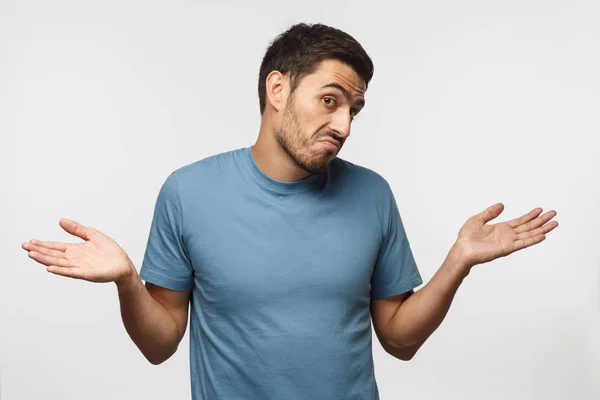 Young man isolated on gray background, showing helpless gesture with arm and hands, mouth curved as if he does not know what to do. I don't know.