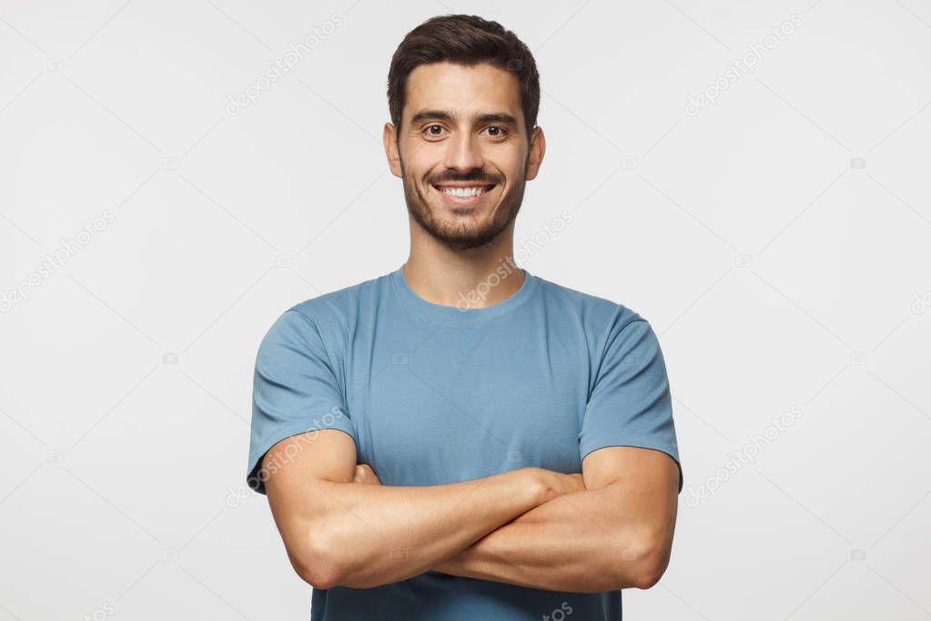 Smiling handsome man in blue t-shirt standing with crossed arms isolated on gray background