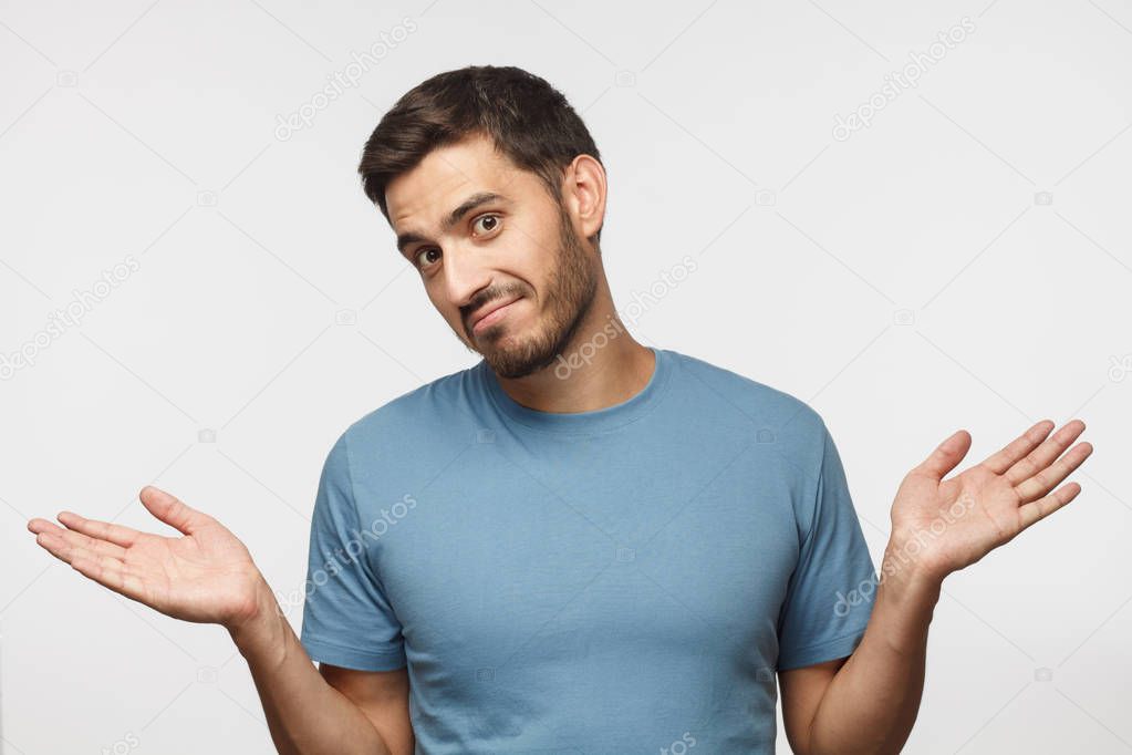I don't know. Portrait of young confused man in blue t-shirt standing and shrugging shoulders, spreading hands isolated on gray background. I dunno