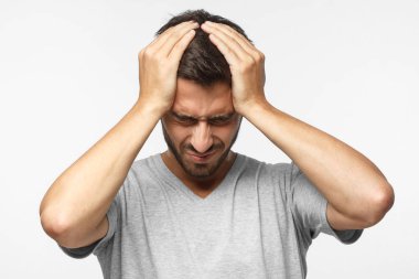 Ne kadar onun başım ağrıyor gösterilen, ağrı, sefil ve yorgun görünümlü gri arka plan üzerinde izole genç adam. Baş ağrısı kavramı. 