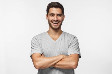 Çapraz kolları üzerinde gri arka plan izole olan mavi t-shirt ayakta yakışıklı gülen portre