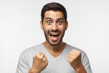 Young man shouting while his team win, raised both fist in victory gesture, isolated on gray background. Casual soccer fan concept clipart