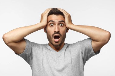 Şok içerik. Bağırarak, kafasını iki eliyle tutarak Gri tişört sürpriz genç erkek