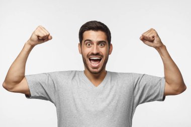 Genç adam onun takım kazanmak bağırarak zafer jest, gri arka plan üzerinde izole içinde her iki yumruk kaldırdı