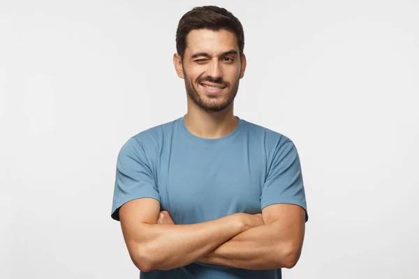 笑顔やウインク 交差の腕を持つ シャツでハンサムな若い男は 灰色の背景に分離カメラ目線 — ストック写真