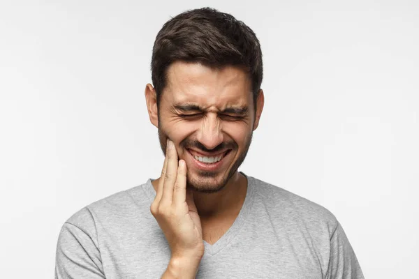 Toothache concept. Indoor shot of young man feeling pain, holding his cheek with hand, suffering from bad tooth ache