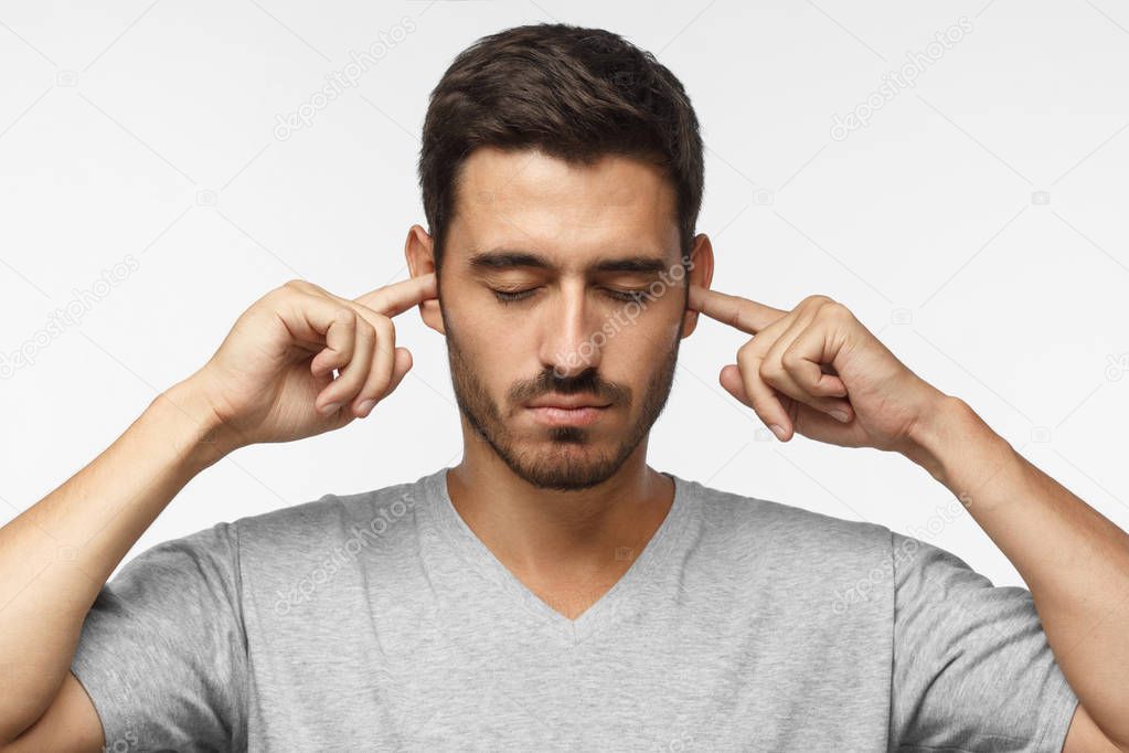  Loud music problem. Young man covering ears, trying to avoid hearing loud noise