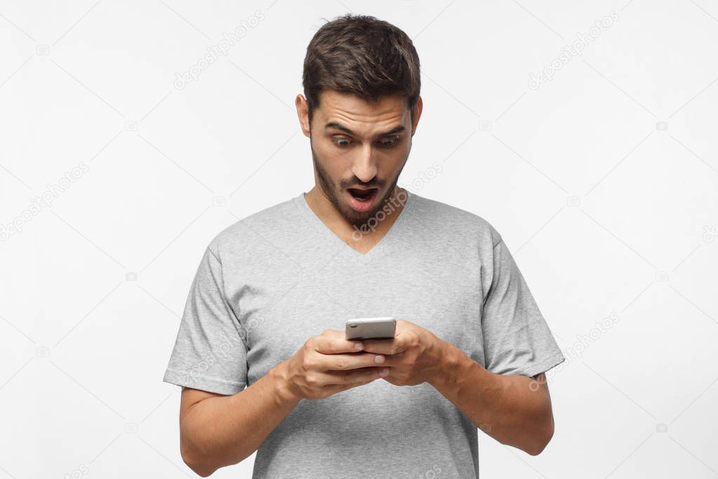 Portrait of young male impressed by media content from web on display of her smartphone,  isolated on gray background. Shock content concept