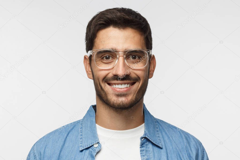 Close up shot of smiling handsome man in blue denim shirt and trendy trasparent glasses isolated on gray background
