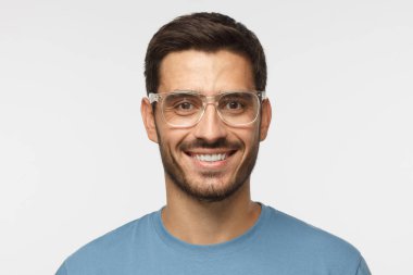 Modern güzel adam gri arka plan üzerinde izole mavi t-shirt ve trendy trasparent gözlük gülümseyen