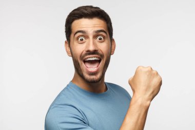 Tutkulu futbol hayranı. Ekibi kazanırken, rahat mavi t-shirt çığlık içinde genç adam yumruk zafer jest, gri arka plan üzerinde izole olarak ortaya çıkar