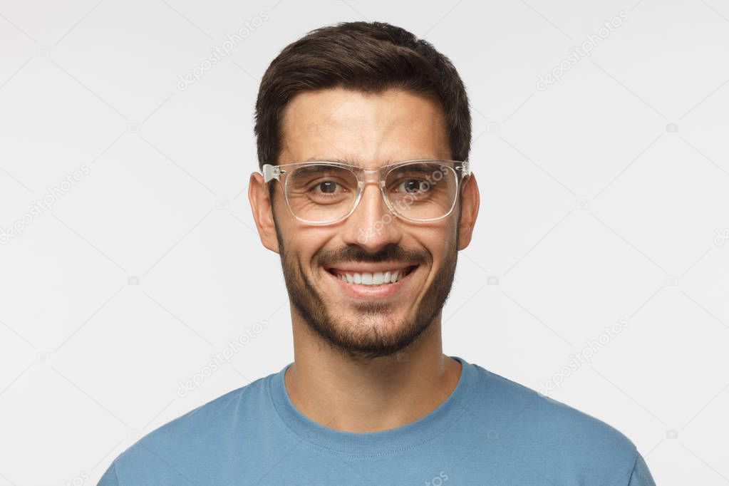 Smiling modern nice guy in blue t-shirt and trendy trasparent eyeglasses isolated on gray background