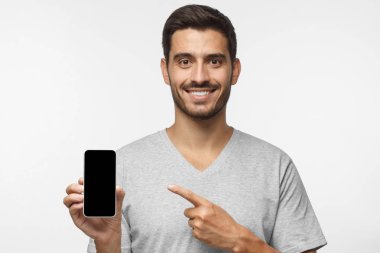 Yakışıklı adam akıllı telefon sunulması ve boş siyah telefon ekranında için app, gri arka plan üzerinde izole kopya alanı ile işaret parmağı ile işaret gri t-shirt
