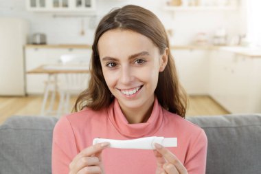 Hamilelik testi holding, güzel gülümseme ile kameraya bakarak, evde kanepede oturan genç mutlu erkek