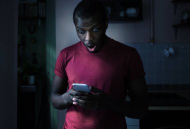 Afrika adam her iki ellerini, ekranda gördüğü ile tamamen sürpriz cep telefonu tutan mutfakta ayakta