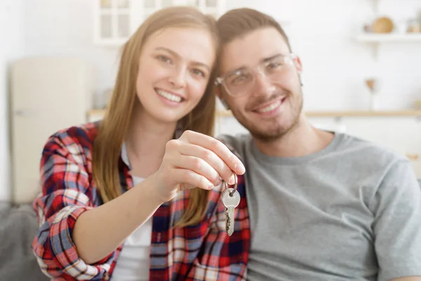 Happy couple holding keys together, sitting on couch at home. Mortgage for young family.