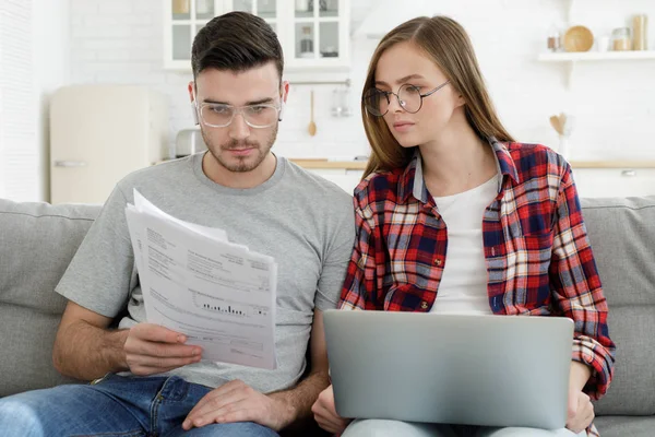 紧张的夫妇看着沮丧 没有钱还清债务 管理家庭预算一起 坐在沙发上在厨房用大量的文件和笔记本电脑 — 图库照片