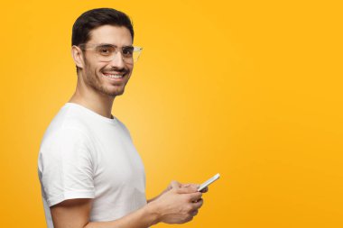 Smartphone açık pozitif gülümseme ile elinde tutan sarı arka plan üzerinde izole genç yakışıklı beyaz adam portresi yan