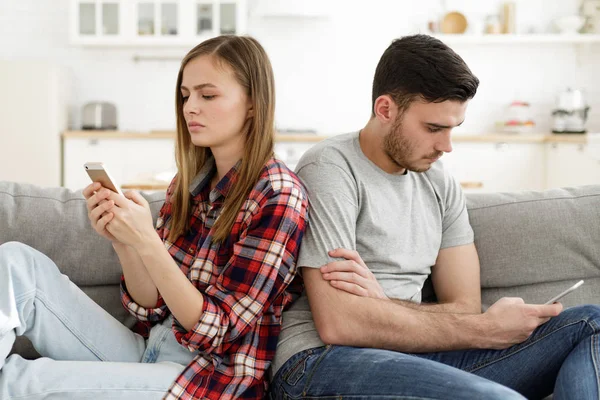 一对夫妇坐在家里的沙发上 在恋爱中遇到了问题 每个人都盯着自己的智能手机看 看上去很累 很困惑 很沮丧 — 图库照片