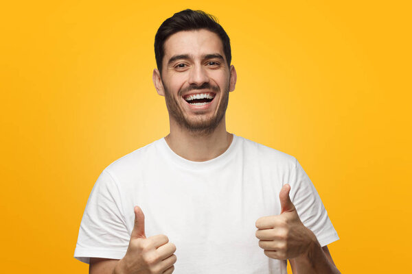 Young laughing man showing thumbs up, isolated on yellow background. Concept of satisfaction with quality and recommendation
