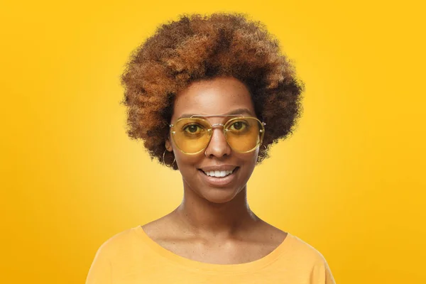 Studio portrait of young smiling african american  woman wearing trendy sunglasses, isolated on yellow background