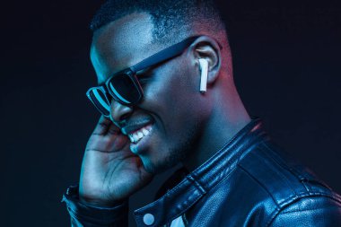 Neon portre Afrika adam dinleme müzik kulaklık ile gülümseyen genç siyah deri ceket